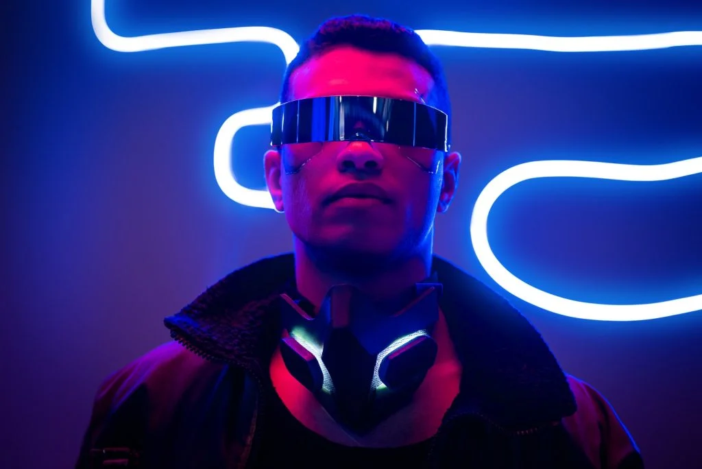 mixed race cyberpunk player in futuristic glasses near blue neon lighting