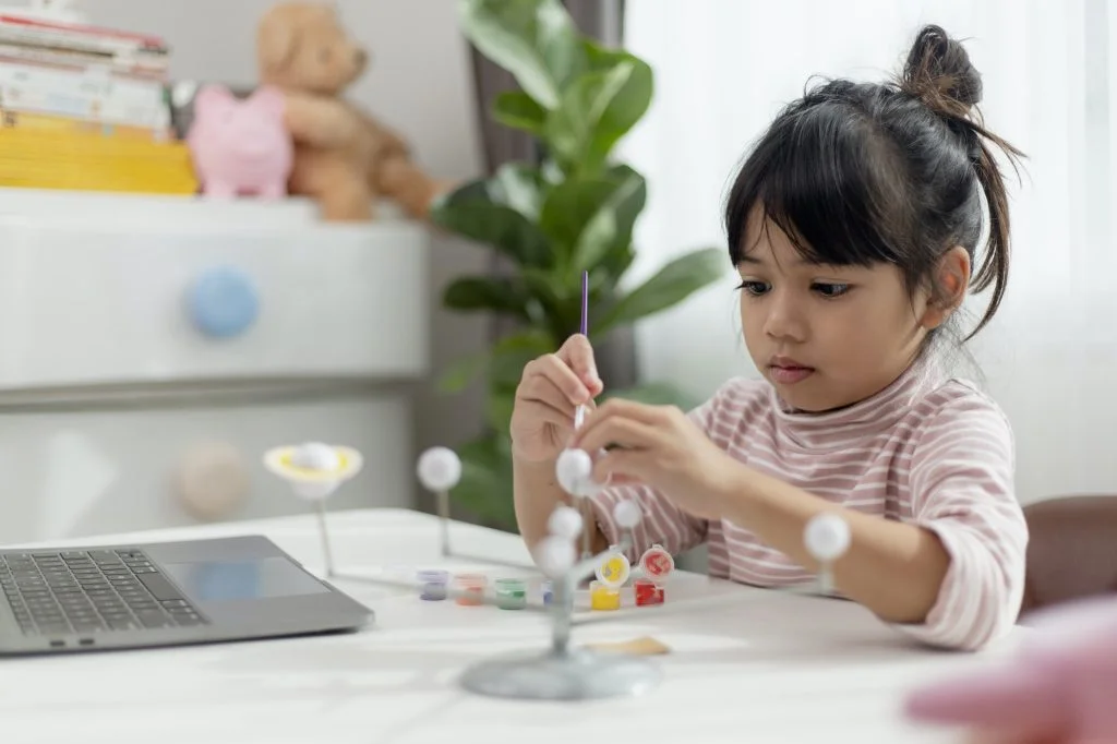 Asian Little girl studies the solar system in geography class. looking at the scale model of planets
