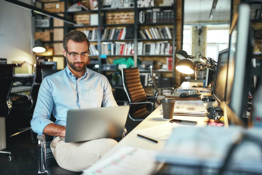 Comfortable workplace. Portrait of young and successful bearded man in eyeglasses working with