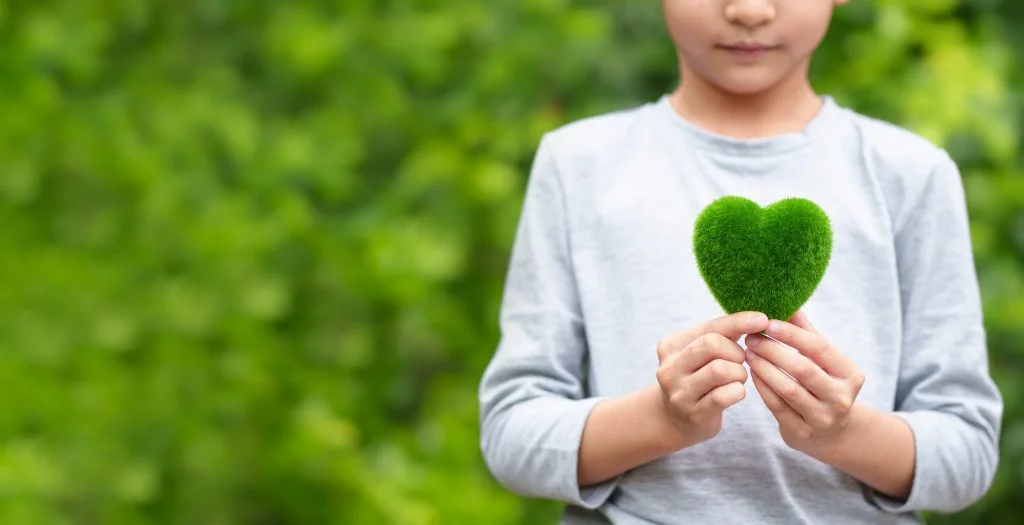Unidentified kid is holding green heart model on green background.