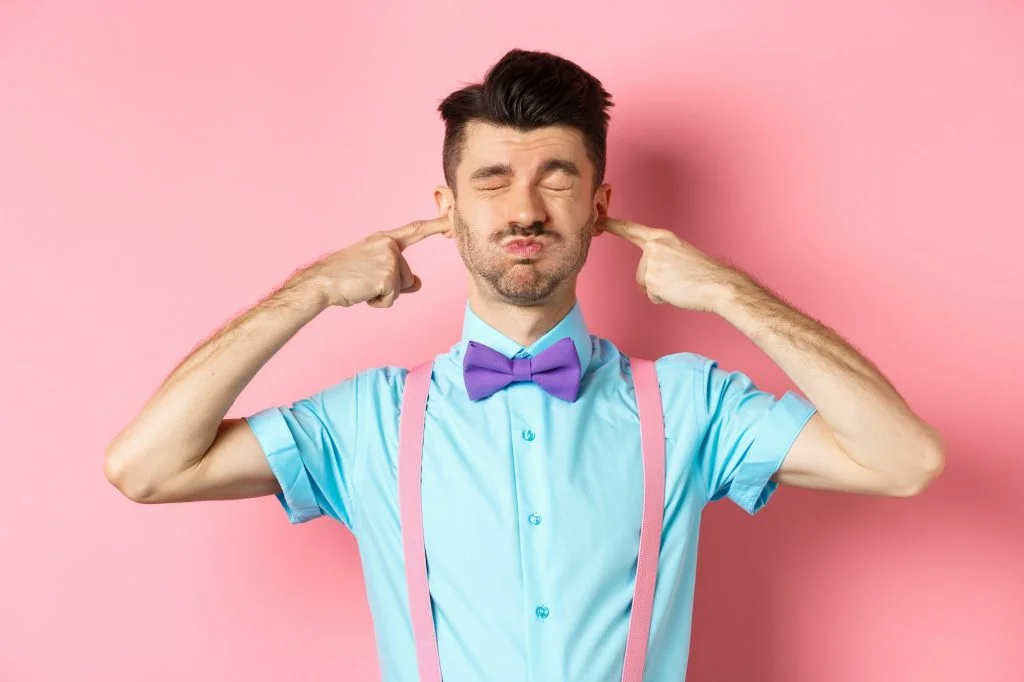 Annoyed funny guy in bow-tie shut ears, plug fingers and grimacing, irritated by loud noise