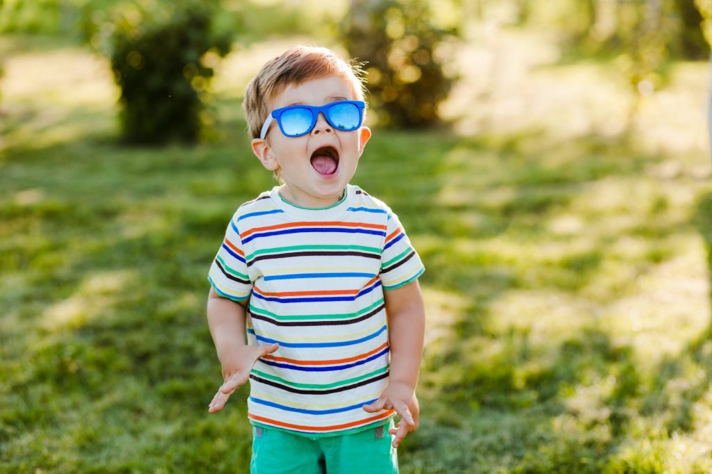 Little cute boy looks surprised in summer garden in bright sunglasses