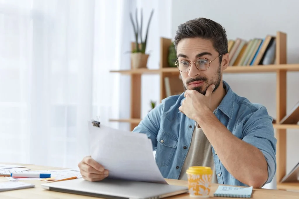 Surprised male office director dressed casually, looks with puzzled expression at payment obligation