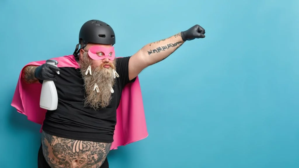 Horizontal shot of serious confident bearded superhero man stretches arm and poses with detergent go