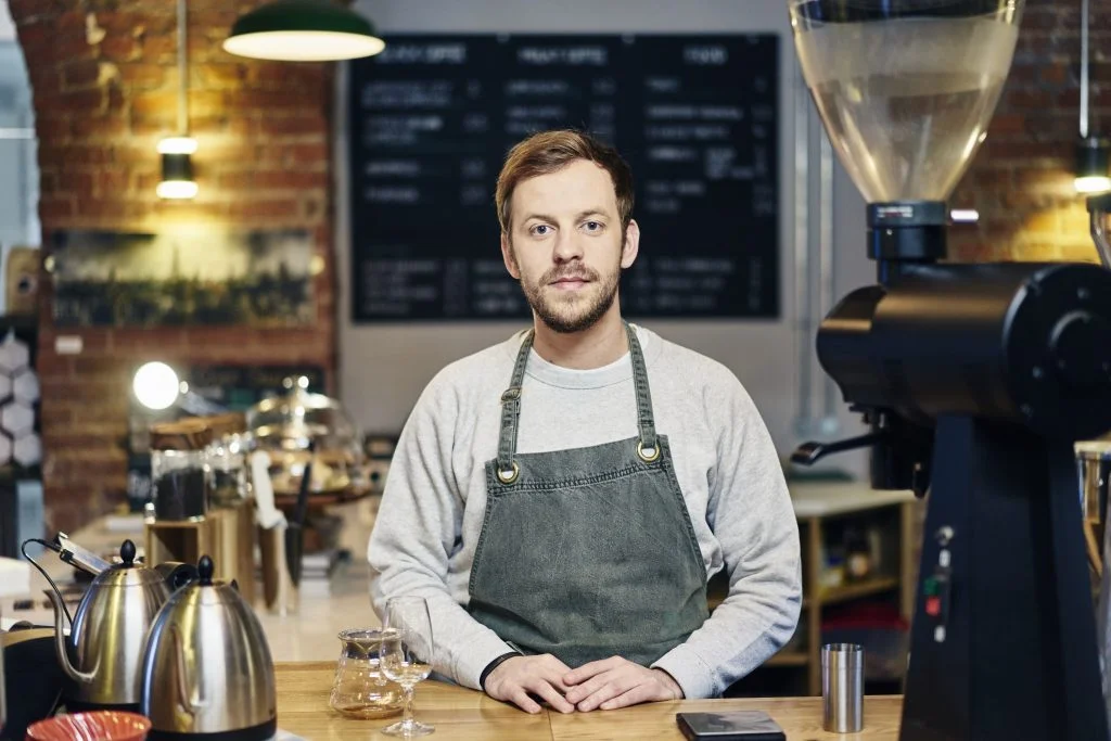 Portrait of young male barista at coffee shop kitchen counter