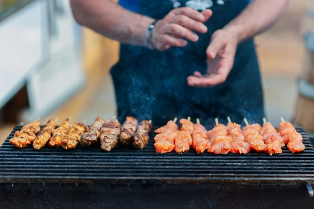 man frying barbecue chicken skewers in the backyard, close-up of hands and barbecue grill